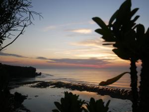 a sunset view of a beach with palm trees at Padang-Padang Inn in Uluwatu