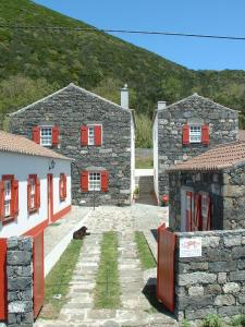 een stenen huis met rode ramen en een hond die ervoor zit bij Casal do Vulcão in Capelo
