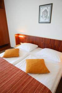 two beds in a hotel room with white sheets and orange pillows at Hotel Donat - All Inclusive in Zadar