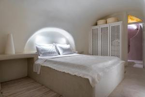 a white bedroom with a bed with an arched ceiling at Christina's Cave House in Fira