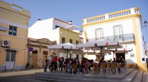 a group of people sitting at an outdoor table with umbrellas at Ana's Apartments in Sines
