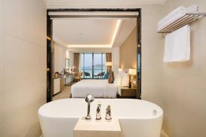 a bathroom with a bath tub and a bedroom at Asteria Comodo Nha Trang Hotel in Nha Trang