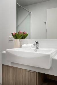 a white bathroom sink with a vase of pink flowers at Quest Midland in Midland Junction