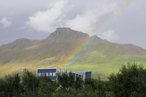 um arco-íris em frente a uma montanha com um edifício em Stuðlaberg em Skagaströnd