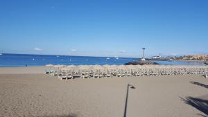 a beach with chairs and umbrellas and the ocean at Torres del Sol Playa de Las Vistas FREE WIFI in Playa de las Americas