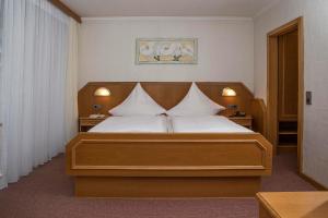 1 dormitorio con cama de madera y almohadas blancas en Kurhotel Unter den Linden, en Bad Füssing