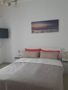 een wit bed met rode kussens en een schilderij aan de muur bij Casa Corona in Capoterra