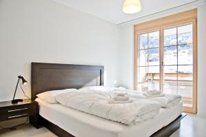 ein großes weißes Bett in einem Zimmer mit Fenster in der Unterkunft Apartment Alpha - GRIWA RENT AG in Grindelwald