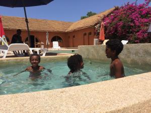 três crianças numa piscina com um guarda-sol em Baobab Lodge em Fadial