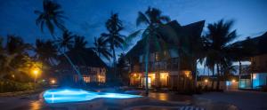 a swimming pool at night with palm trees and a building at Zanziblue in Matemwe