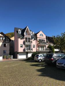 uma casa cor-de-rosa com carros estacionados num parque de estacionamento em Haus Ostermann em Cochem