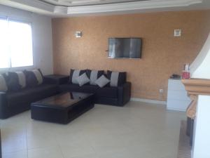 a living room with a black couch and a tv at Garden Beach Sidi Rahal in Sidi Rahal