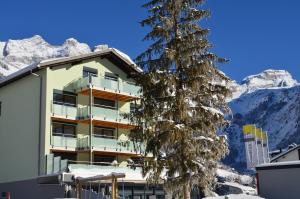 un bâtiment avec un arbre et des montagnes en arrière-plan dans l'établissement Hotel Hahnenblick, à Engelberg
