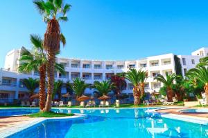 a swimming pool with palm trees in front of a hotel at Hello Yasmine Hotel in Hammamet