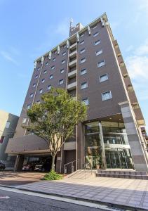 ein hohes Gebäude mit einem Baum davor in der Unterkunft Imabari Urban Hotel (New Building) in Imabari