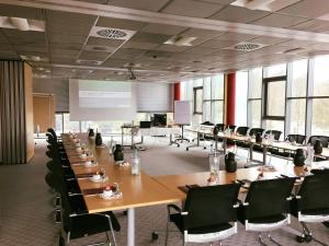una sala de conferencias con mesas y sillas y una pantalla de proyección en Hotel Sternzeit en Wegberg