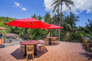 two tables and chairs with red umbrellas on a deck at Maha Guru Huts in Nusa Lembongan