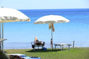 a person sitting in a chair under an umbrella on the beach at Hotel Punta Negra in Alghero