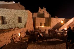 a patio with tables and chairs in a building at night at Albabenshal Lodge Siwa in Siwa