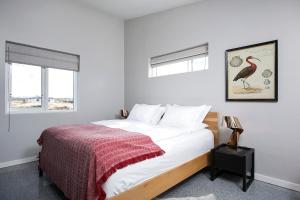 a bedroom with a bed with a red blanket and two windows at Hvassahraun Cabin by the Sea in Vogar