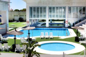 una gran piscina en un edificio con sillas y sombrillas en Suites Puerto Sherry, en El Puerto de Santa María