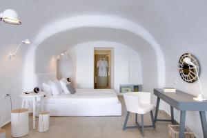 a white bedroom with a white bed and a desk at Santorini Secret Suites & Spa, Small Luxury Hotels of the World in Oia