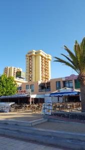 a building with tables and chairs and a palm tree at Playa de las Vistas Los Cristianos WIFI BEACH VIEW in Arona