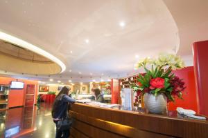 Una donna in piedi al bancone con un vaso di fiori di As Hotel Cambiago a Cambiago