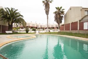 a swimming pool in front of a building with palm trees at TerraBahia Residences in Bahia Inglesa