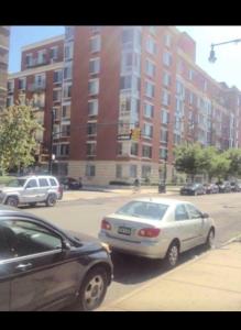 twee auto's geparkeerd aan de kant van een stadsstraat bij Harlem Brownstone in New York