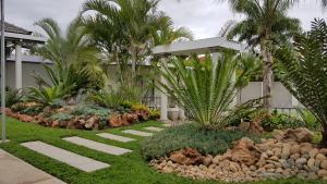 a garden with rocks and palm trees and a house at Dive Inn Guesthouse in Pongola