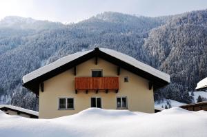 een huis bedekt met sneeuw met bergen op de achtergrond bij Aktiv-Ferienwohnungen Montafon in Sankt Gallenkirch