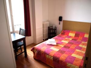 a bedroom with a bed with a colorful quilt and a desk at Hôtel Chateaubriand in Dijon