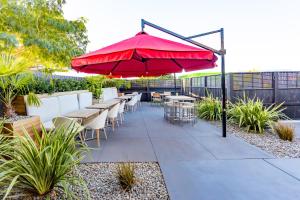 eine Terrasse mit Tischen, Stühlen und einem roten Regenschirm in der Unterkunft The Redwood Hotel in Christchurch