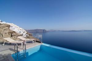a swimming pool with chairs on the edge of the water at Santorini Secret Suites & Spa, Small Luxury Hotels of the World in Oia