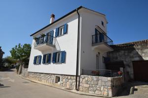 a white building with blue windows and a stone wall at Apartments Celebrini in Malinska