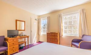 um quarto com uma cama, uma secretária e uma televisão em Marton Guest House em St Peter Port