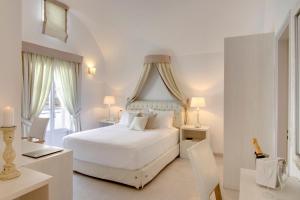 a white bedroom with a white bed and a desk at Santorini Secret Suites & Spa, Small Luxury Hotels of the World in Oia