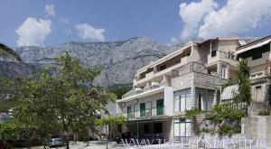 a large white building with a mountain in the background at VILA MILENKA Apartmani Drago in Tučepi