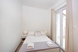 a white bedroom with a bed and a window at Apartments Frado in Novalja