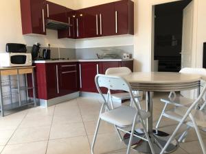 une cuisine avec des placards rouges, une table et des chaises dans l'établissement La Résidence du Cap, au Lavandou