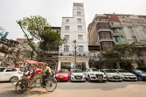 un hombre montando una bicicleta por una concurrida calle de la ciudad con coches en Serenity Diamond Hotel, en Hanói