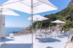 a patio with tables and white umbrellas and the ocean at Casa Mao in Amalfi