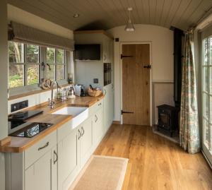 a kitchen with white cabinets and a wooden floor at Luxury Shepherds Hut in Bransgore
