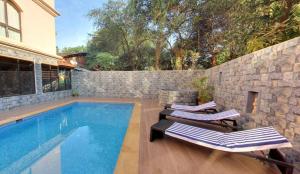 a swimming pool with two lounge chairs next to a stone wall at Calangute Grande in Calangute