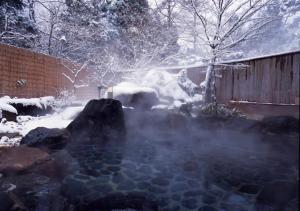 a hot spring with snow in a yard with a fence at Higashiyama Park Hotel Shinfugetsu in Aizuwakamatsu