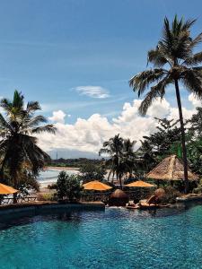 a swimming pool with palm trees and a beach at Puri Dajuma Beach Eco-Resort & Spa in Pulukan