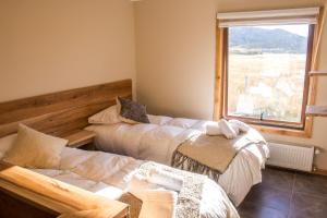 two beds in a room with a window at Hostal El Puestero in Puerto Natales