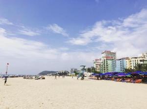 a beach with people and blue umbrellas and buildings at Khách sạn Hồ Gươm in Sầm Sơn