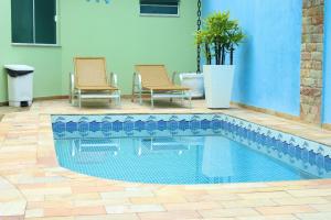 a swimming pool next to two chairs and a house at Pousada Maré dos Sonhos in Itanhaém
